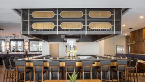 A modern bar area with a central island, bar stools, and a wooden table with a potted plant.