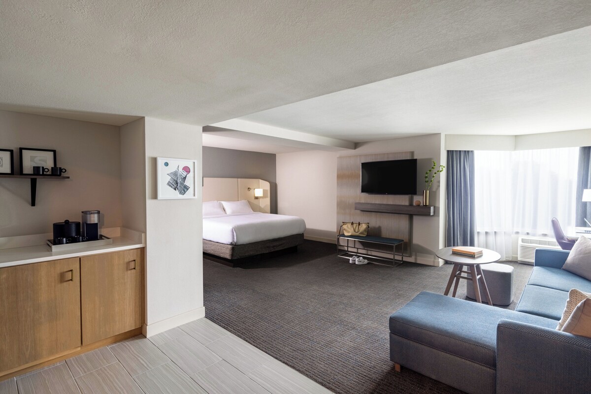 A modern hotel room with a bed, a sofa, a TV, and a small table.