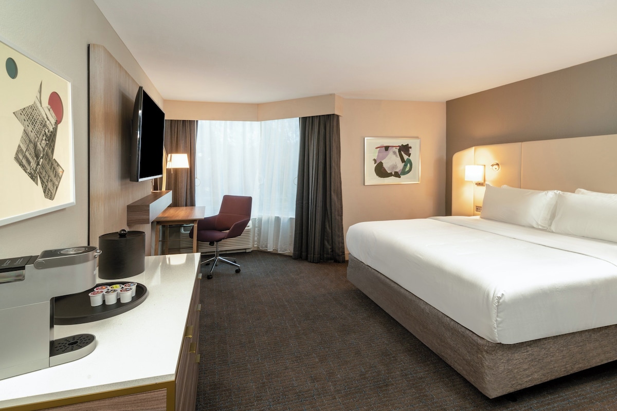 Quarto de hotel com cama, escrivaninha, cadeira, televisão e máquina de café.