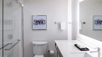 A modern bathroom with a glass shower enclosure, a toilet, a sink with a mirror, and a framed picture on the wall.