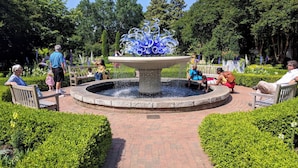 A circular brick pathway with a central fountain surrounded by benches and greenery.