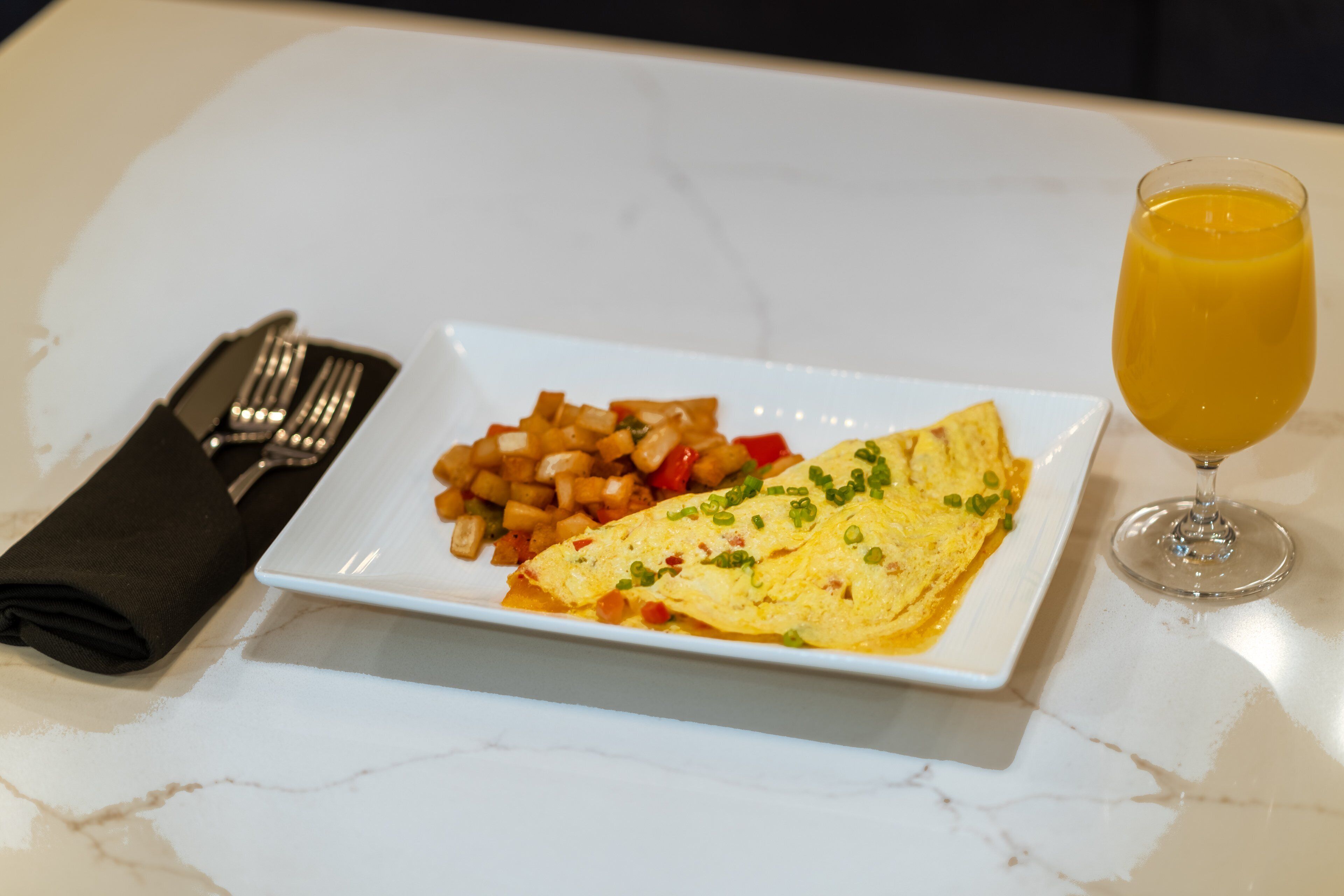 A white plate with an omelette, diced vegetables, and a glass of orange juice on a marble table.