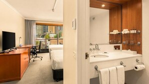 A hotel room with a desk, two beds, a large mirror, and a view of the city. - Sydney Harbour Hotel (The Rocks)