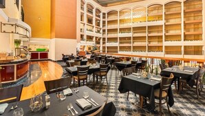 A hotel lobby with multiple dining tables, a central bar area, and a large seating area with a patterned floor. - Sydney Harbour Hotel (The Rocks)