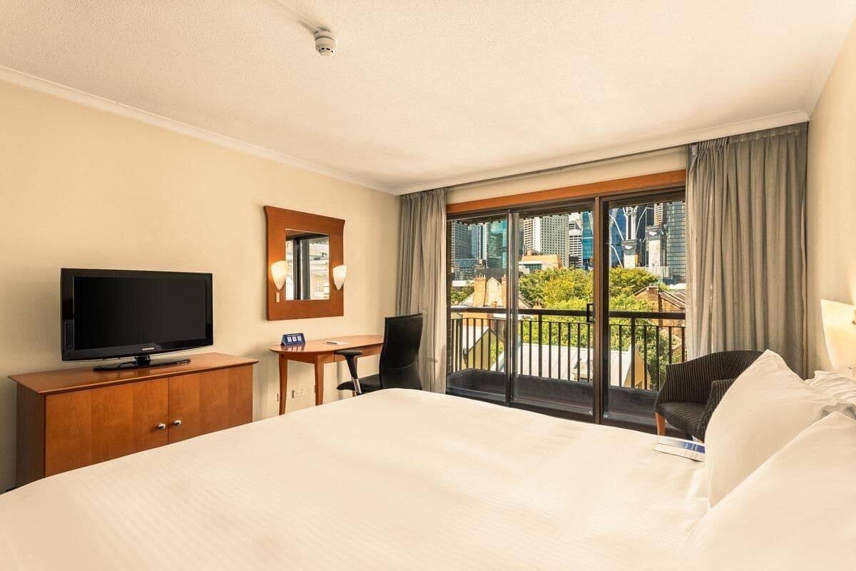 A hotel room with a bed, a TV, a desk, and a balcony with a city view.