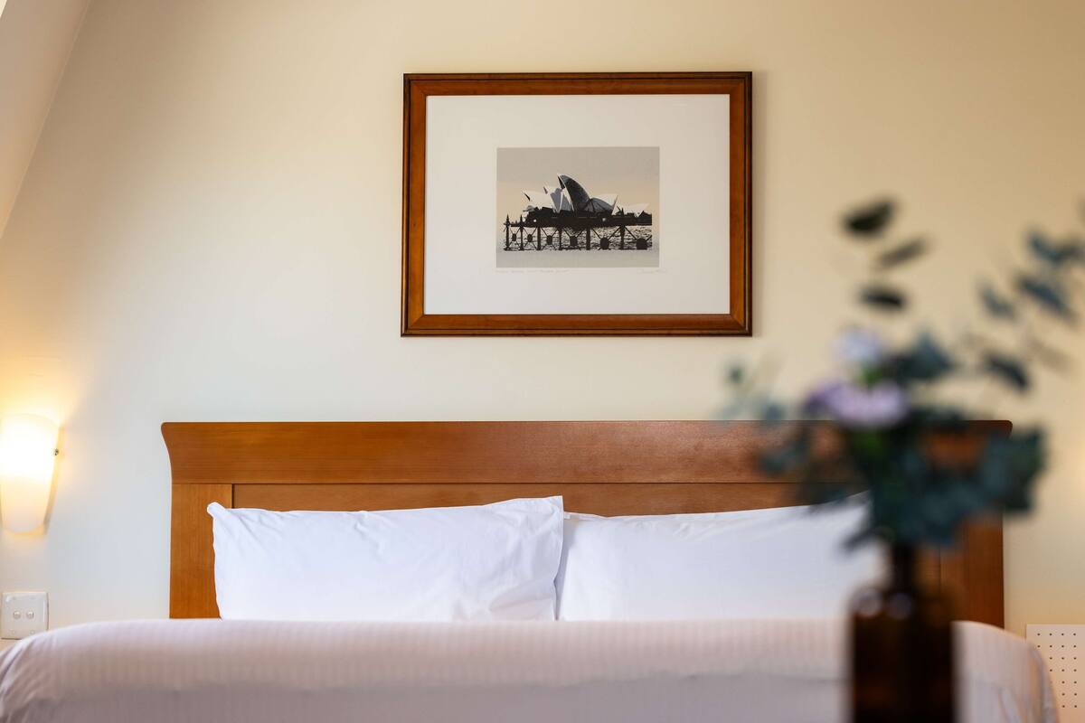 A neatly made bed with white linens, a wooden headboard, and a framed picture of a building on the wall.