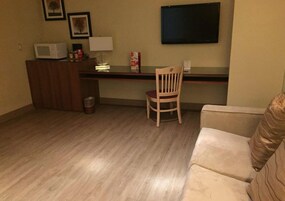 Un espacio habitable pequeño y funcional con suelo de madera, un escritorio con computadora y lámpara, una silla y un sofá.