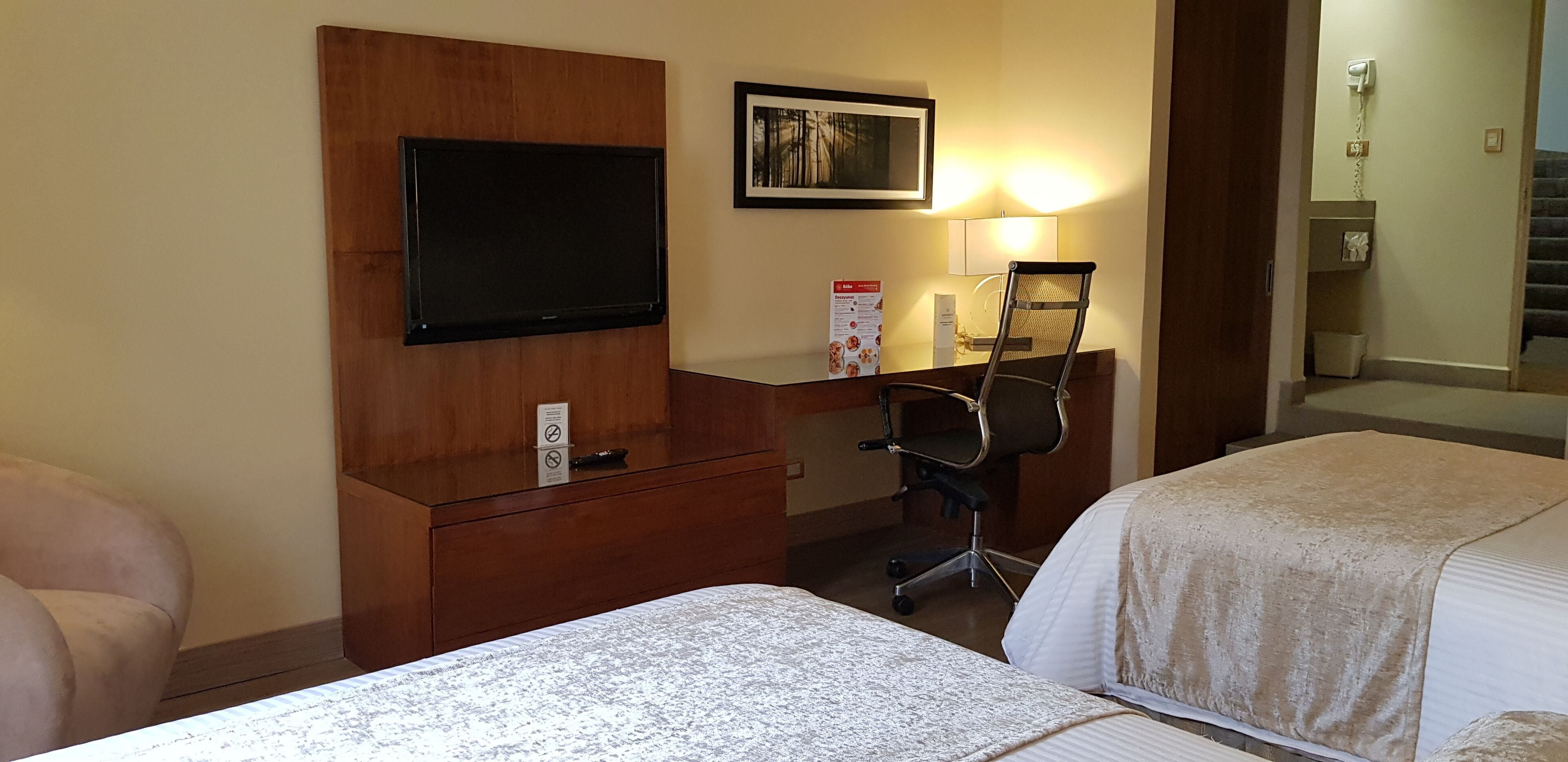 A hotel room with two beds, a desk with a chair, a television, and a framed picture on the wall.