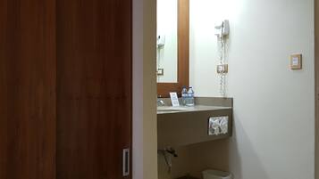 Un baño con puerta de madera, espejo, secador de pelo, lavamanos y dispensador de toallas.