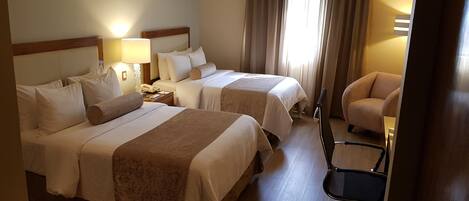 Habitación de hotel con dos camas, un escritorio, una silla y una lámpara.
