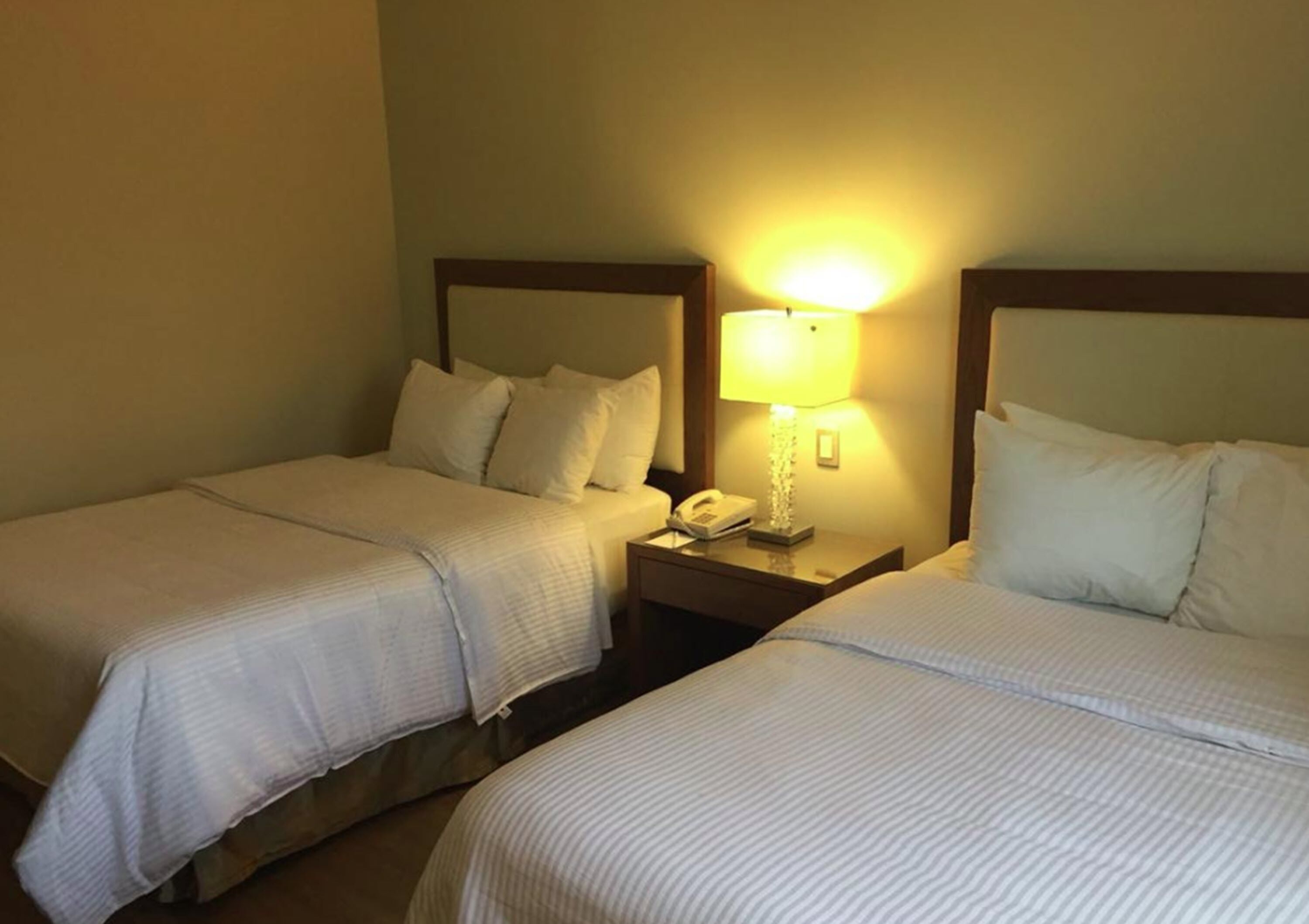 A hotel room with two single beds, each with a wooden headboard, a bedside table with a lamp, and a telephone.