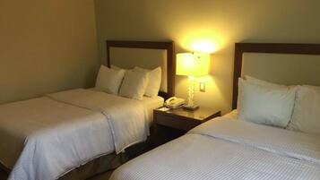 A hotel room with two single beds, each with a wooden headboard, a bedside table with a lamp, and a telephone.