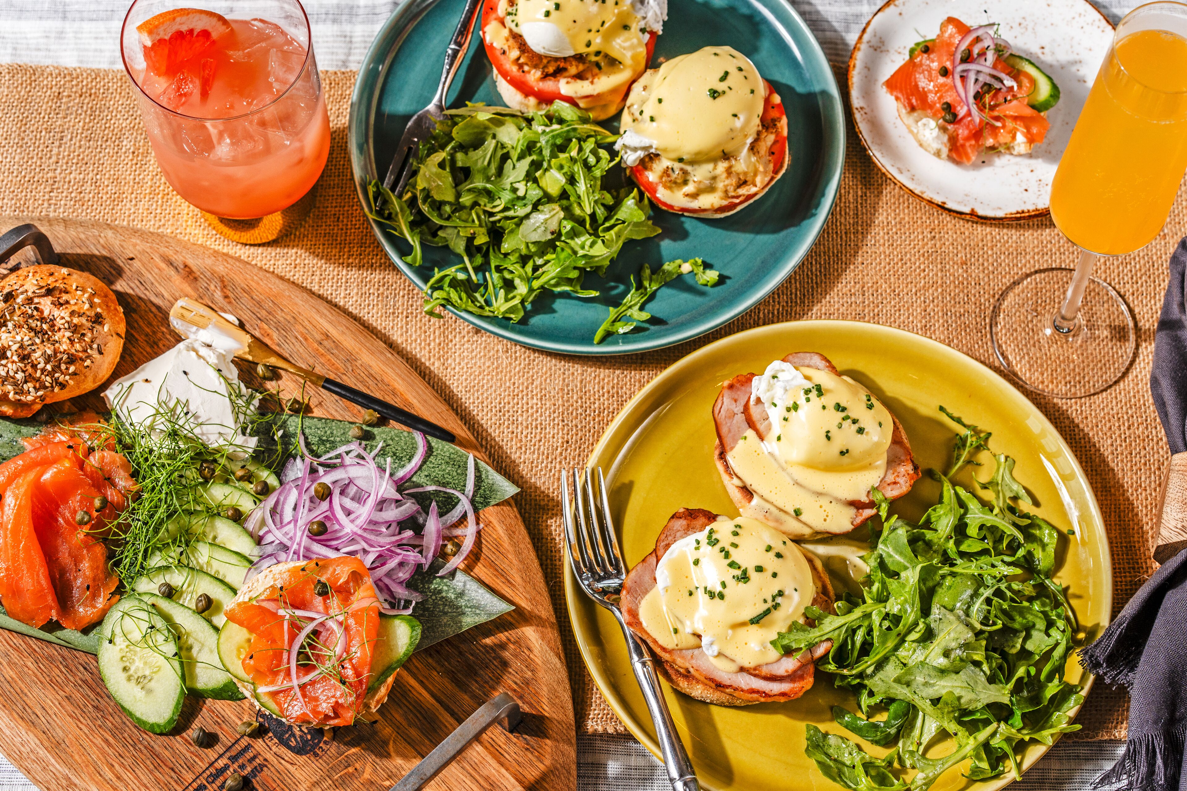 A variety of dishes including eggs benedict, smoked salmon, and a salad, suggesting a breakfast setting.