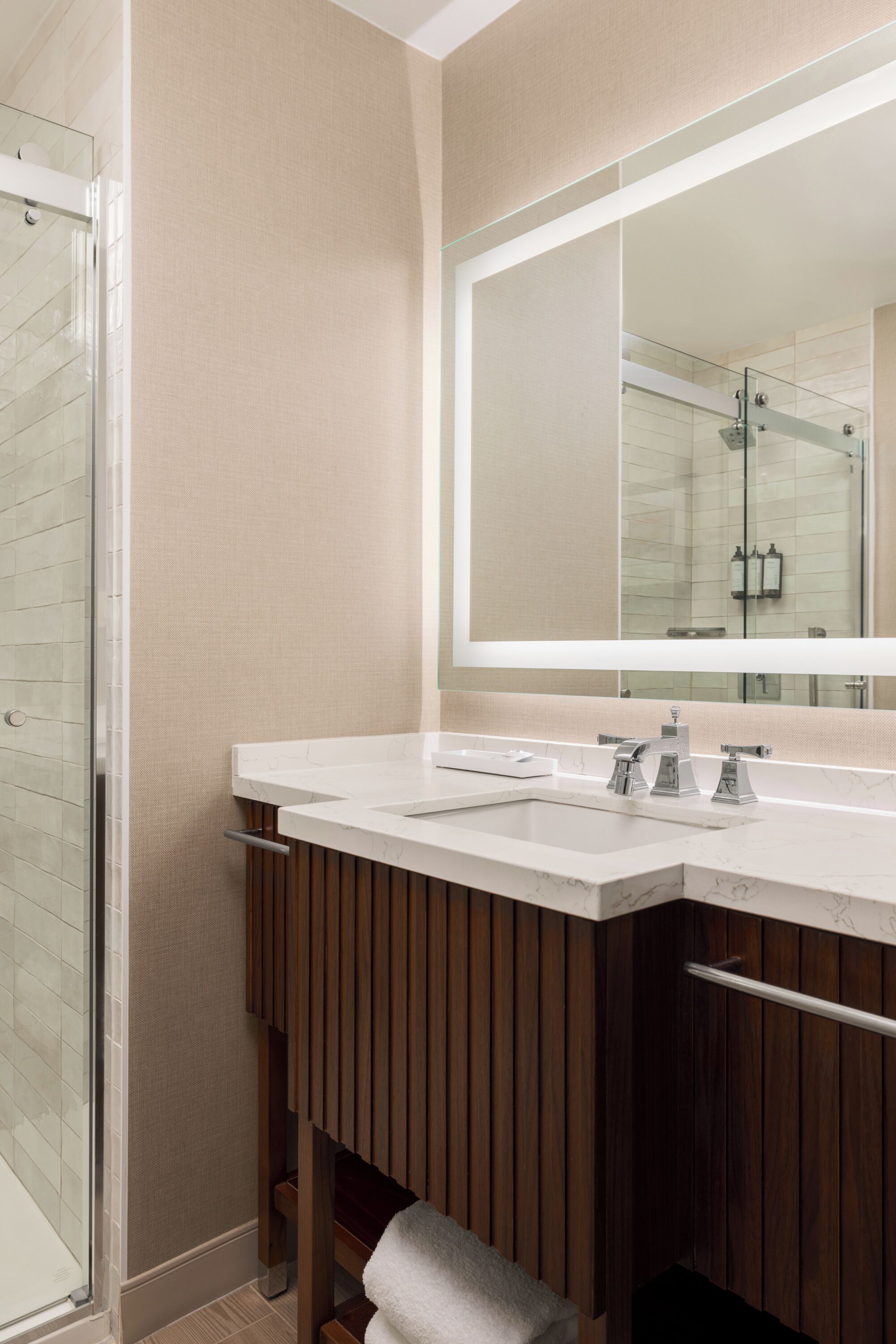A modern bathroom with a glass shower enclosure, a large mirror, and a wooden vanity with a towel rack.