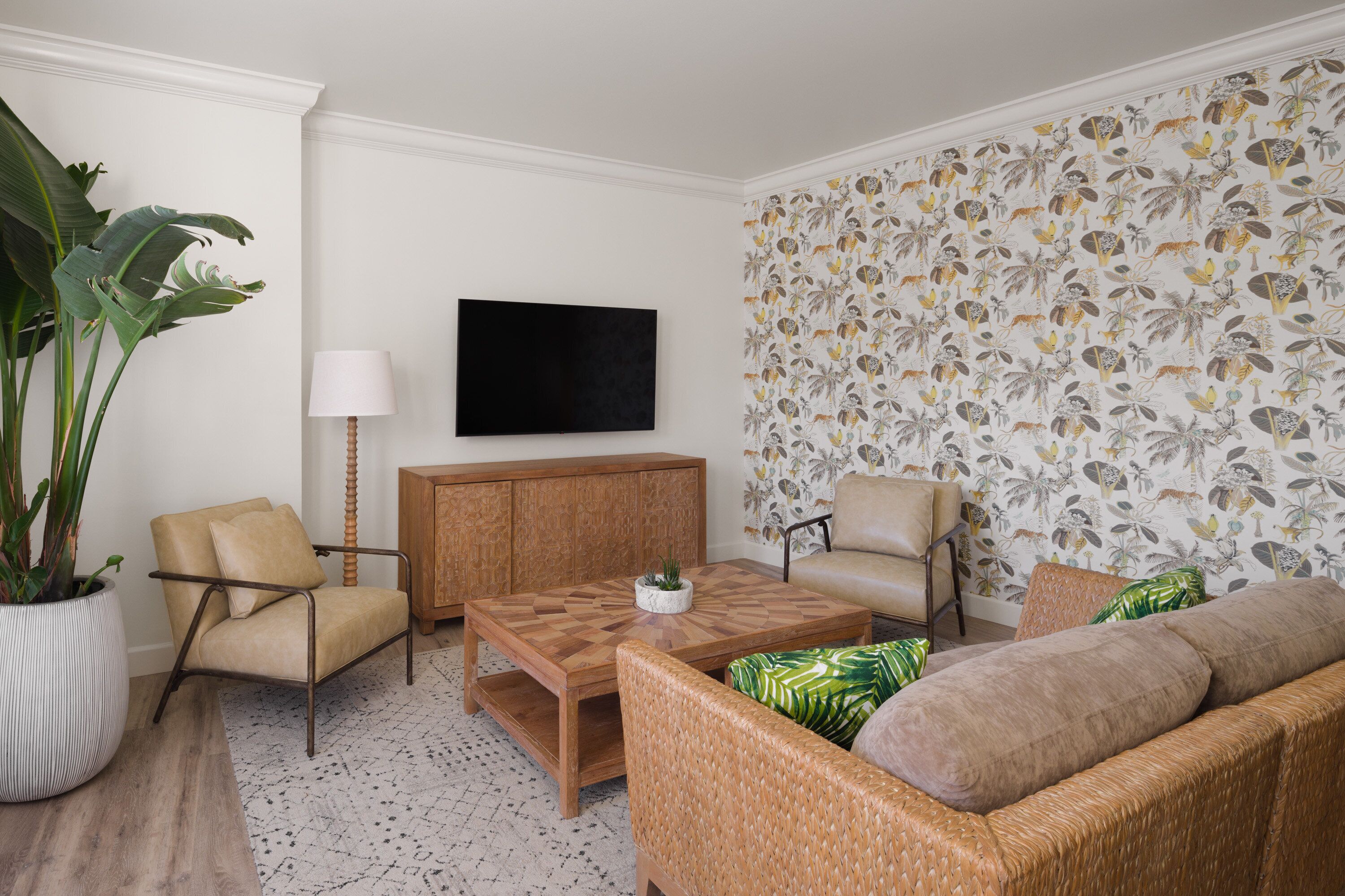 A living room with a sofa, two armchairs, a coffee table, a TV, a cabinet, and a large plant.