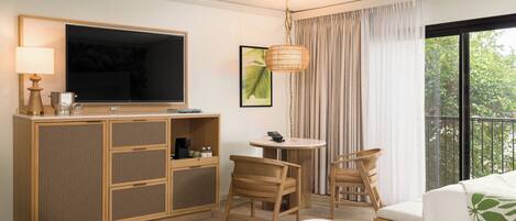 A hotel room with a bed, a TV, a desk with a lamp, a chair, a small table, and a balcony with curtains.