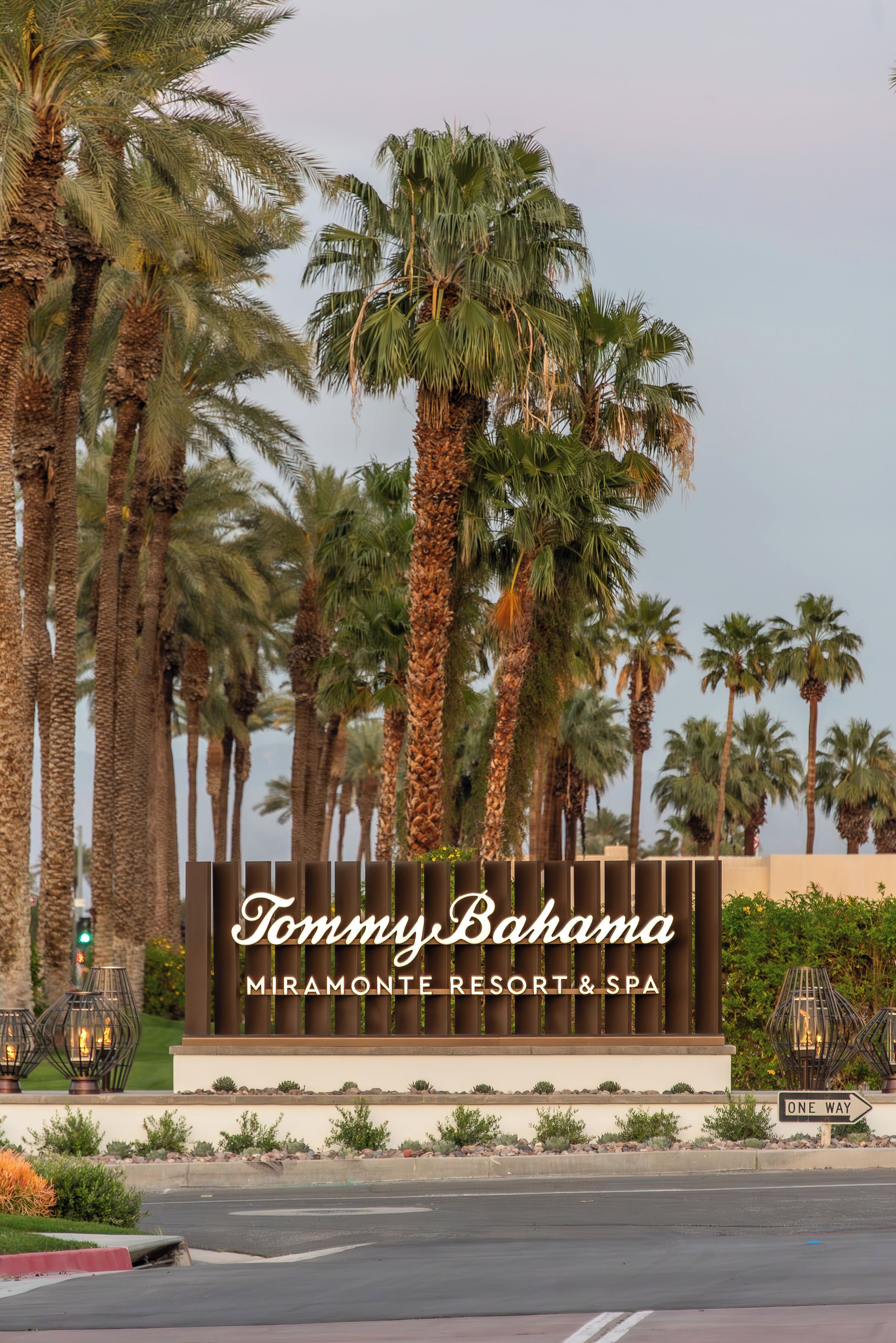 A sign for Tommy Bahama Miramonte Resort & Spa with a one-way street sign and palm trees in the background.