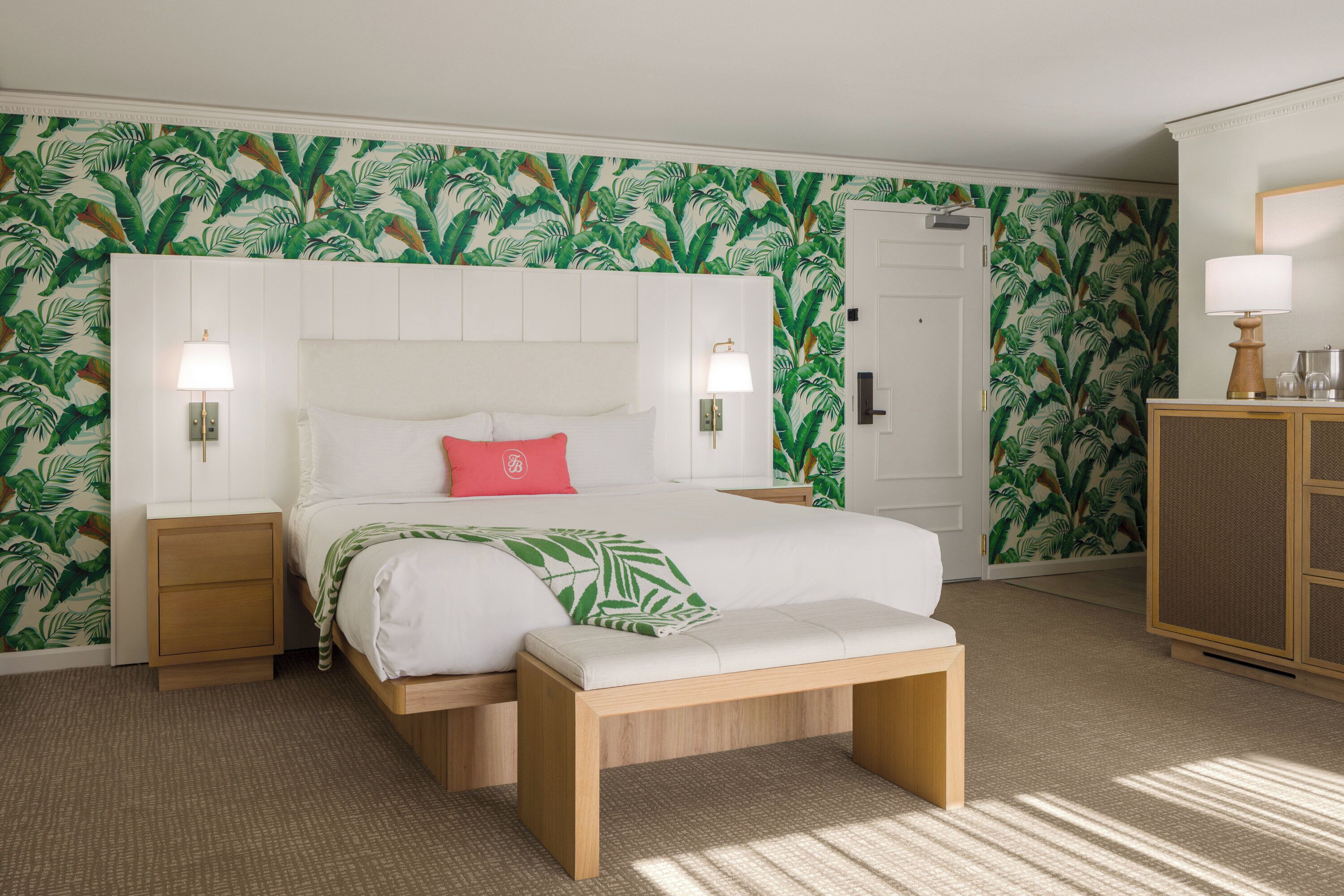 A bedroom with a large bed, a bench, a nightstand, a dresser, and a door.