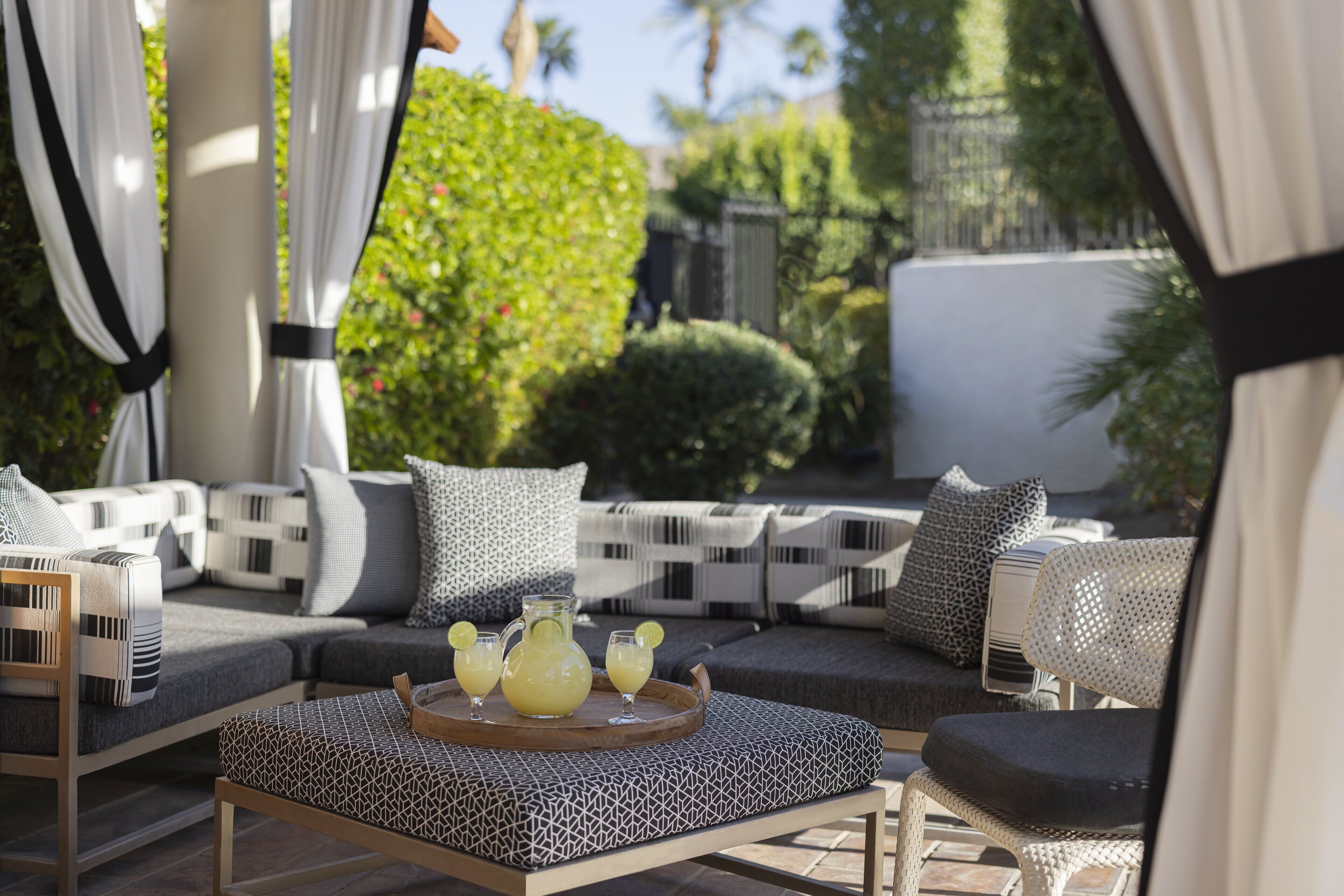 A sunlit outdoor seating area with a sofa, chairs, and a tray with drinks.