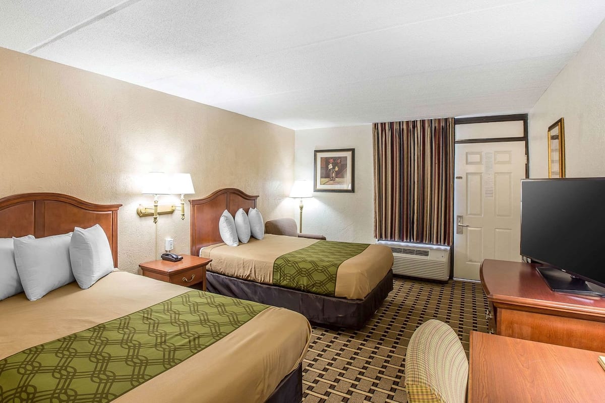 Ein Hotelzimmer mit zwei Betten, einem Fernseher, einem Schreibtisch und einem Sessel.
