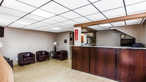 A reception area with a wooden reception desk, two leather chairs, a small table with a vase of flowers, and a clock on the wall. - Econo Lodge Savannah Midtown (Savannah)