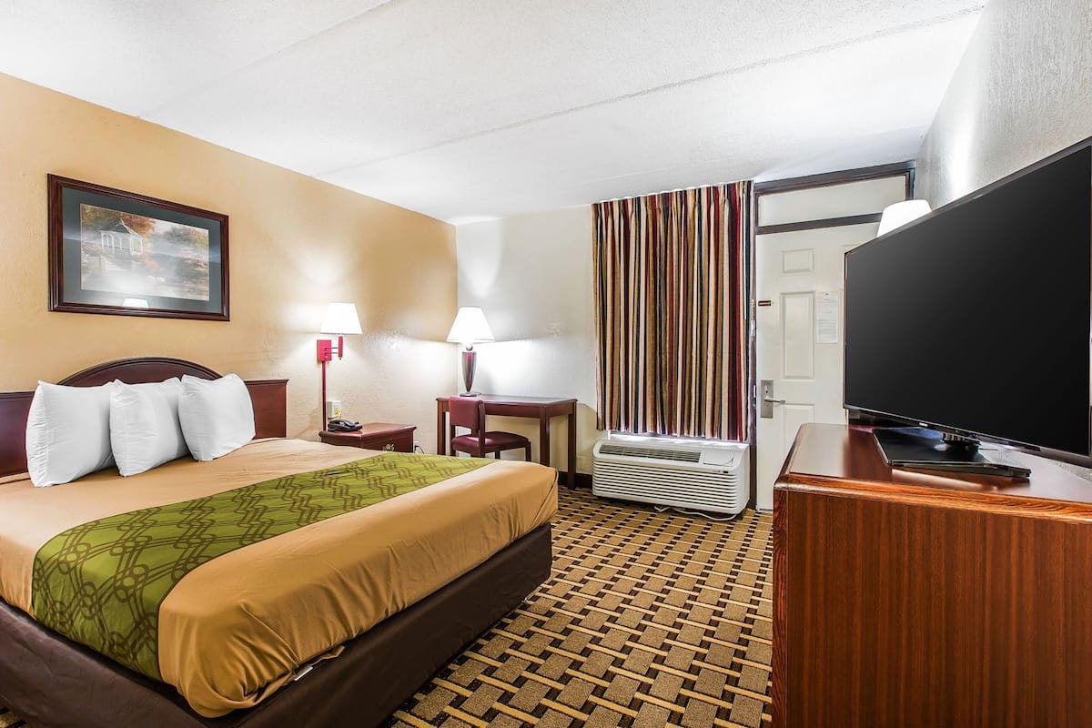 Ein Hotelzimmer mit Bett, Schreibtisch, Fernseher, Heizung und einem Bild an der Wand.