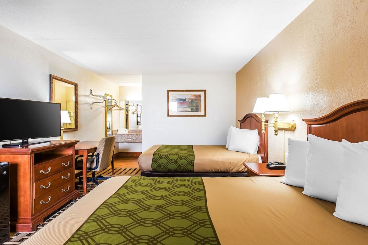 Ein Hotelzimmer mit Bett, Fernseher, Schreibtisch, Stuhl, Lampe und einem Gemälde an der Wand.