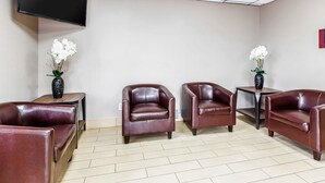 A room with a TV mounted on the wall, two sofas, a small table with a vase of flowers, and a tiled floor. - Econo Lodge Savannah Midtown (Savannah)