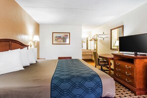 Una habitación de hotel con una cama, un escritorio, un aparador, un televisor y un cuadro en la pared.