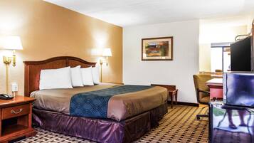 A hotel room with a large bed, two bedside lamps, a desk with a chair, a television, and a framed painting on the wall.