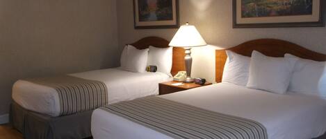 Une chambre d’hôtel avec deux lits, chacun doté d’une tête de lit en bois, d’une table de chevet avec une lampe et de tableaux encadrés accrochés au mur.