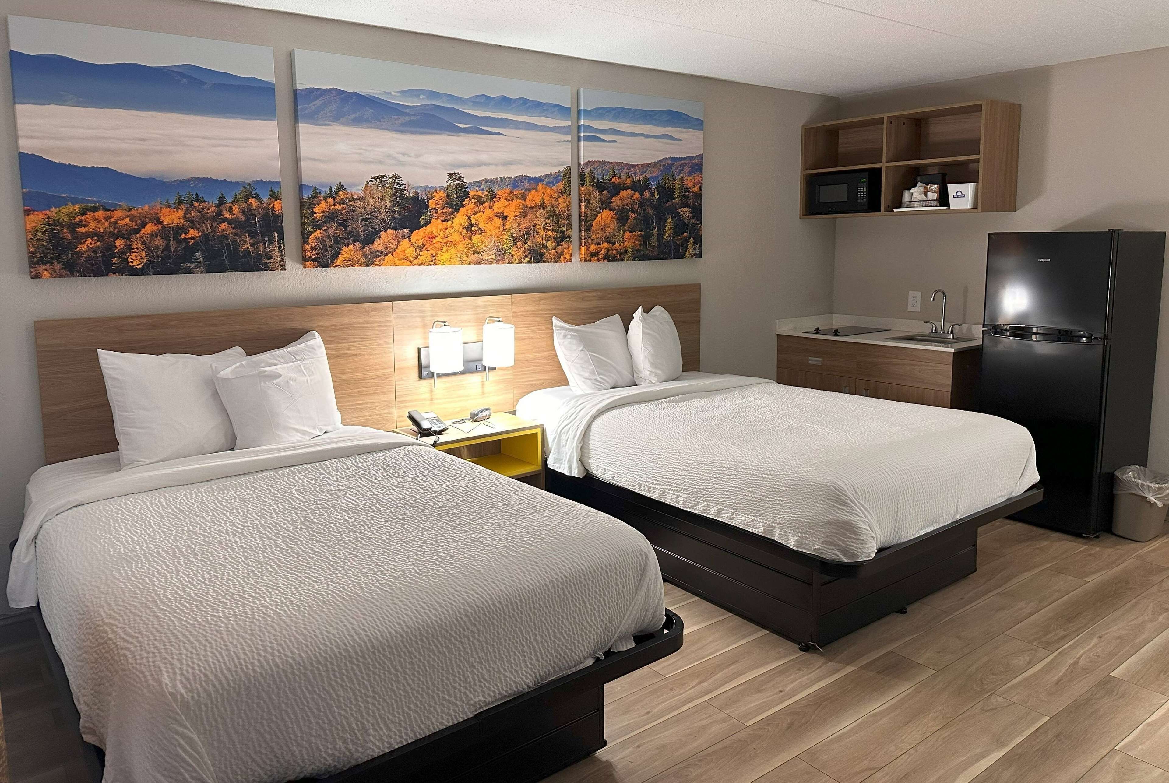 Hotellihuone, jossa on kaksi sänkyä, puinen sängynpääty, pieni työpöytä lampun kanssa, mikroaaltouuni ja jääkaappi.