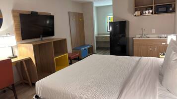 A hotel room with a bed, a desk with a chair, a television, a wardrobe, a microwave, and a refrigerator.