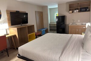A hotel room with a bed, a desk with a chair, a television, a wardrobe, a microwave, and a refrigerator.