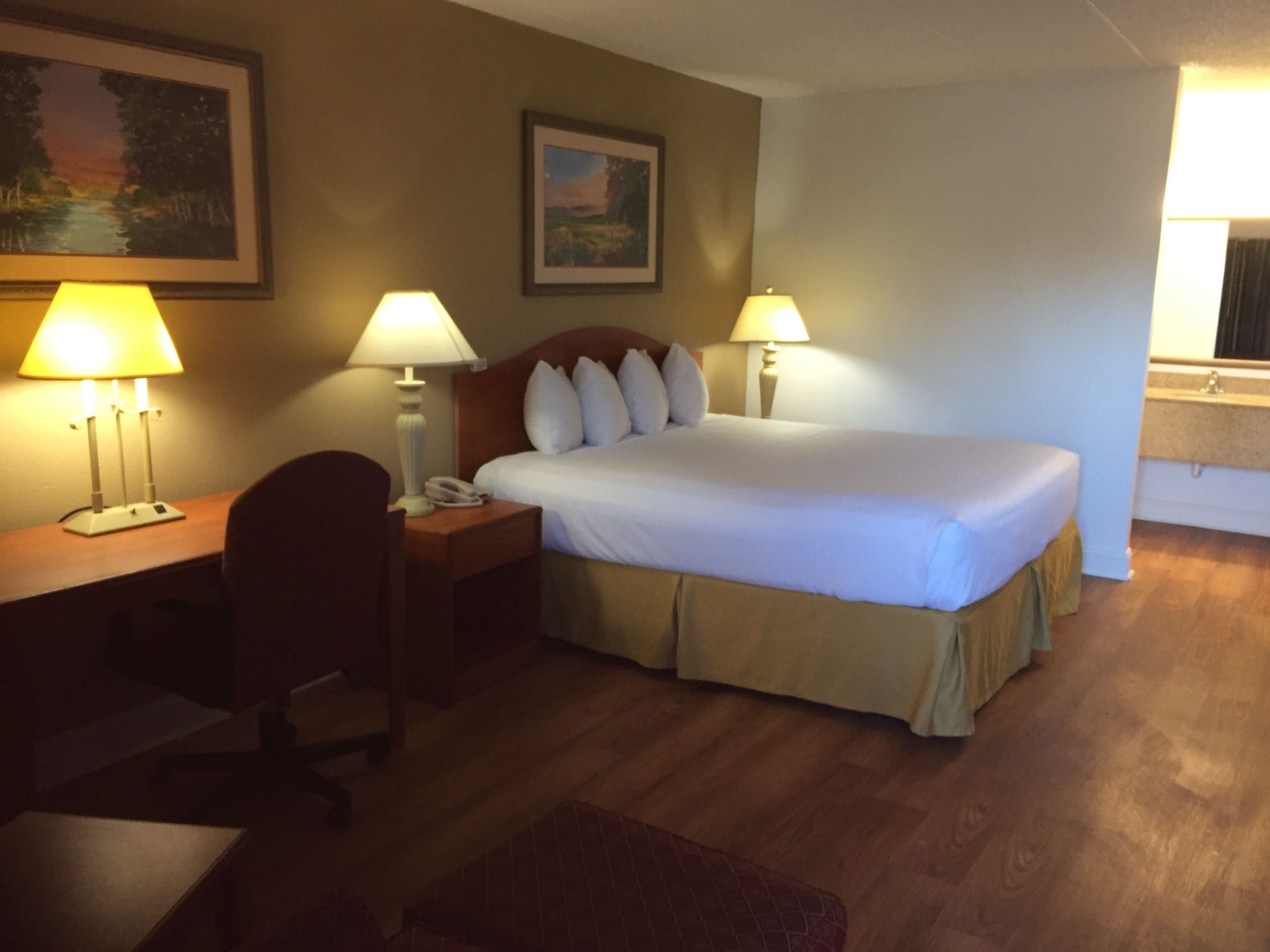 Een hotelkamer met een bed, twee bedlampen, een bureau met telefoon, een stoel en een schilderij aan de muur.