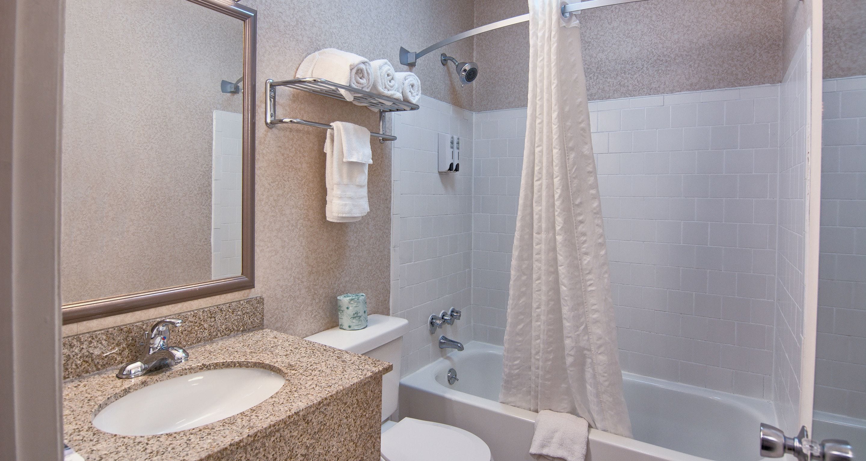 A bathroom with a granite countertop sink, a toilet, a bathtub, and a shower curtain.