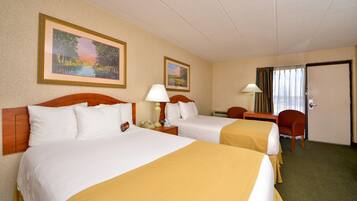 A hotel room with two beds, a desk, a chair, and two framed pictures on the wall.