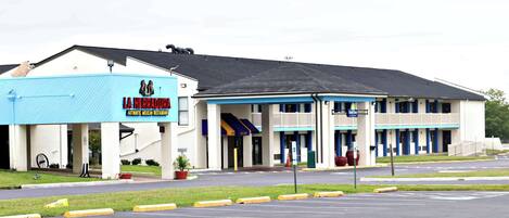 Un motel con fachada azul y blanca, un letrero que dice 'LA HERADURA Auténtico Restaurante Mexicano', y un estacionamiento al frente.