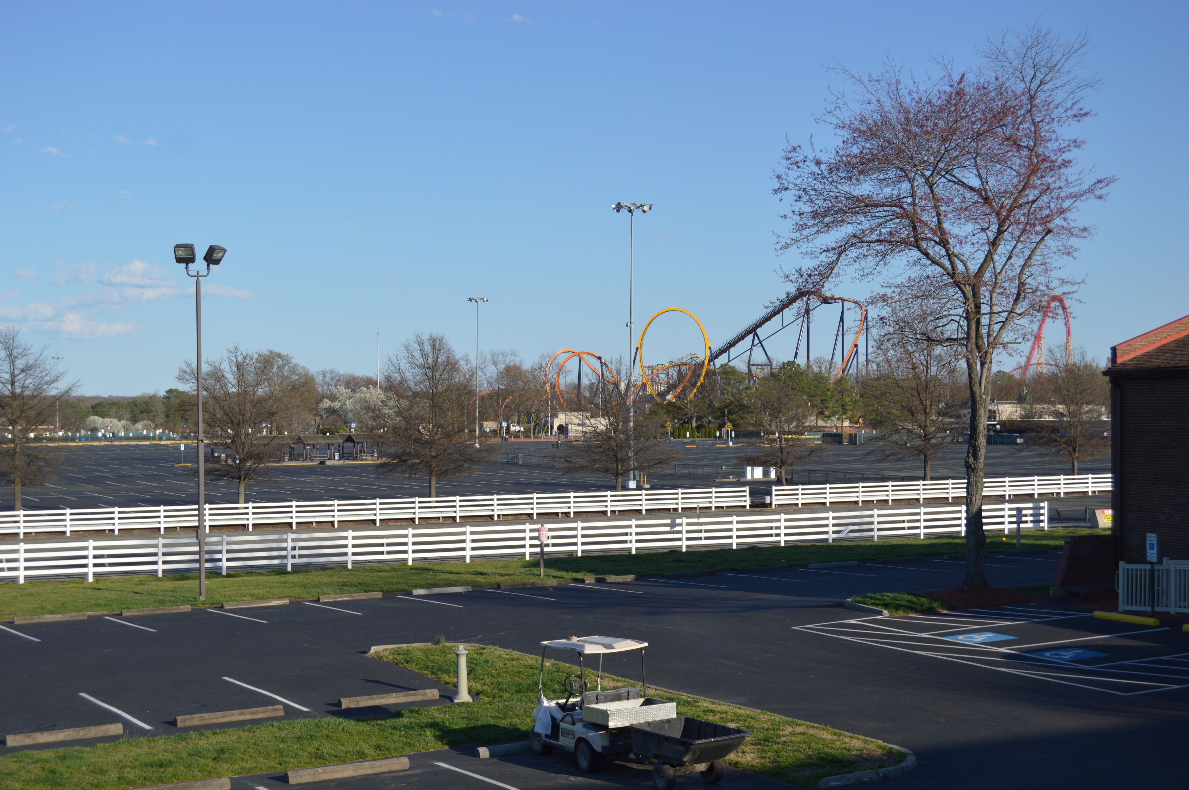 A parking lot with a golf cart, a fenced area, and a roller coaster in the background.
