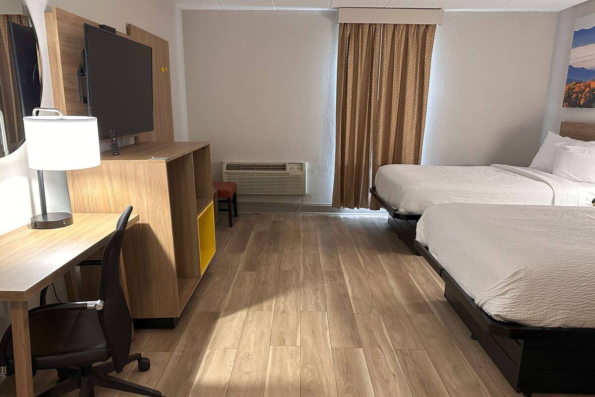 Une chambre d’hôtel avec un bureau en bois, une chaise, un lit et un téléviseur.
