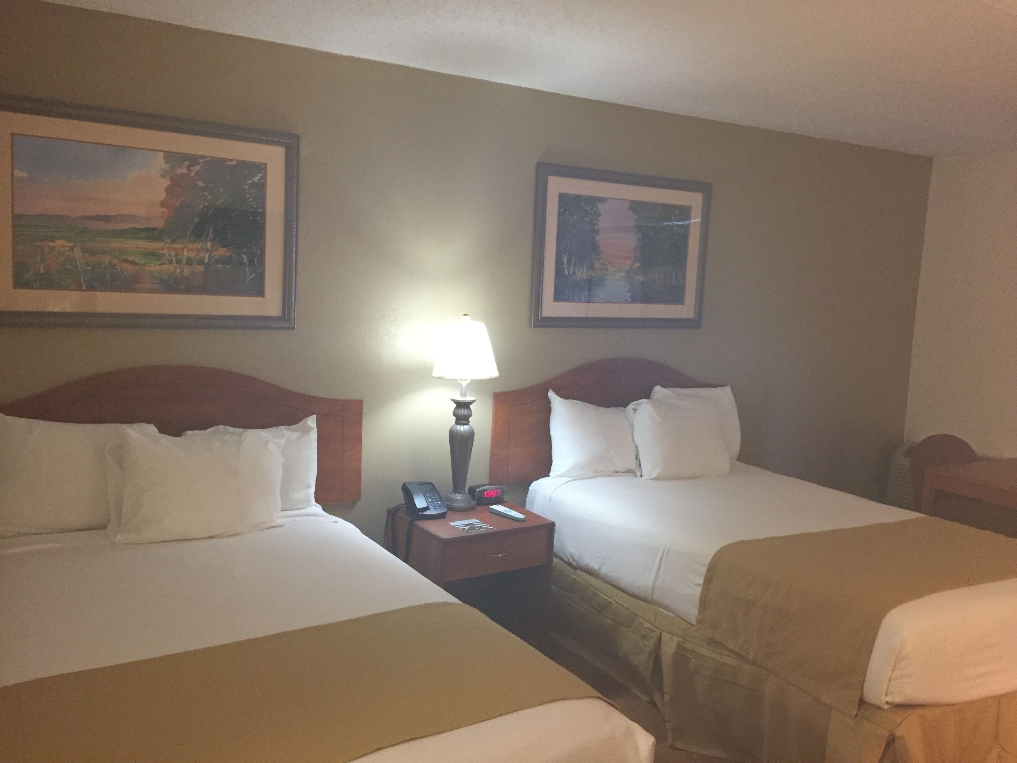 A hotel room with two beds, a nightstand with a lamp, and two framed pictures on the wall.