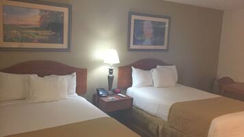 A hotel room with two beds, a nightstand with a lamp, and two framed pictures on the wall.