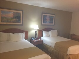 A hotel room with two beds, a nightstand with a lamp, and two framed pictures on the wall.
