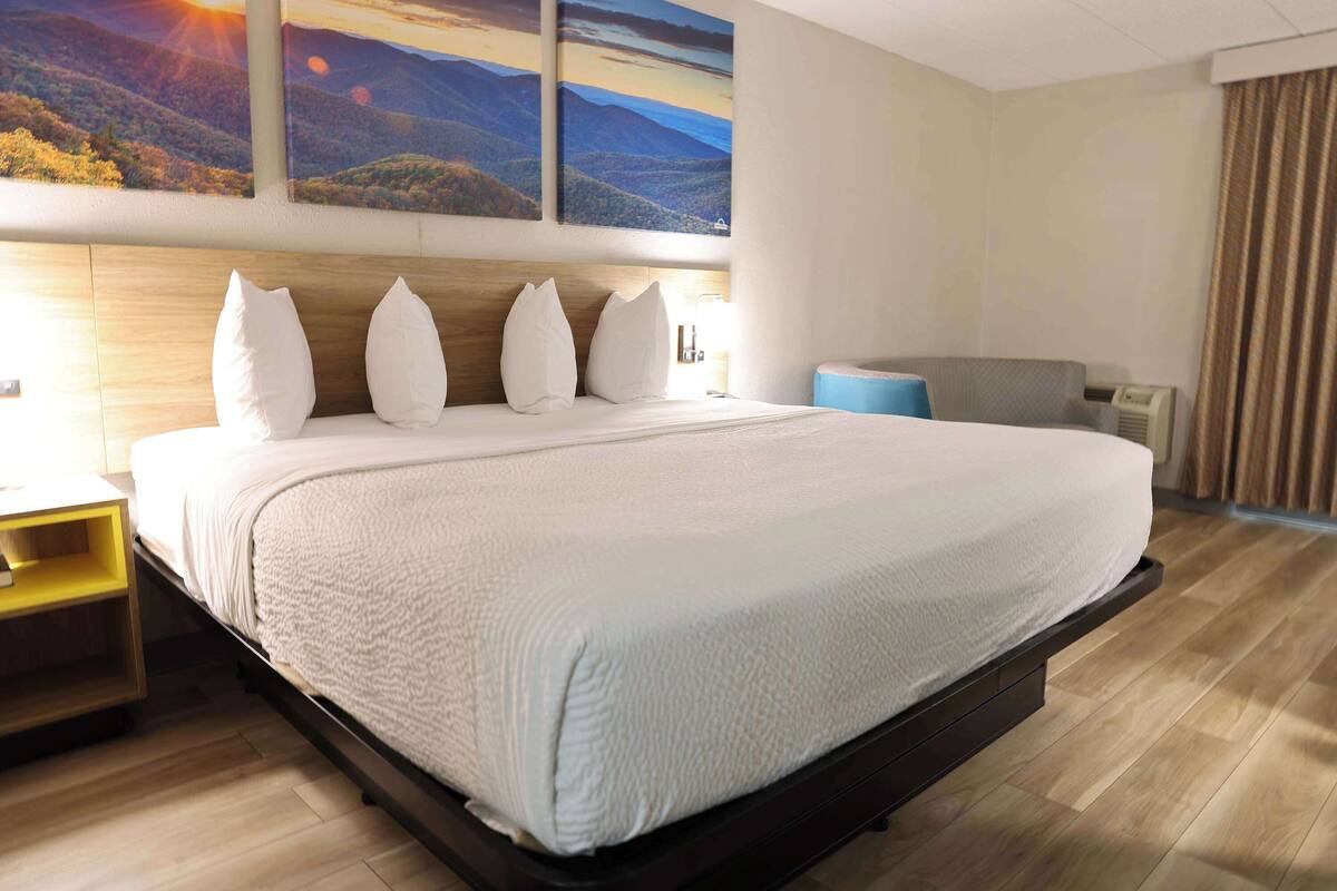 Une chambre d’hôtel avec un grand lit, une table de chevet, un bureau et une vue sur un paysage montagneux par les fenêtres.