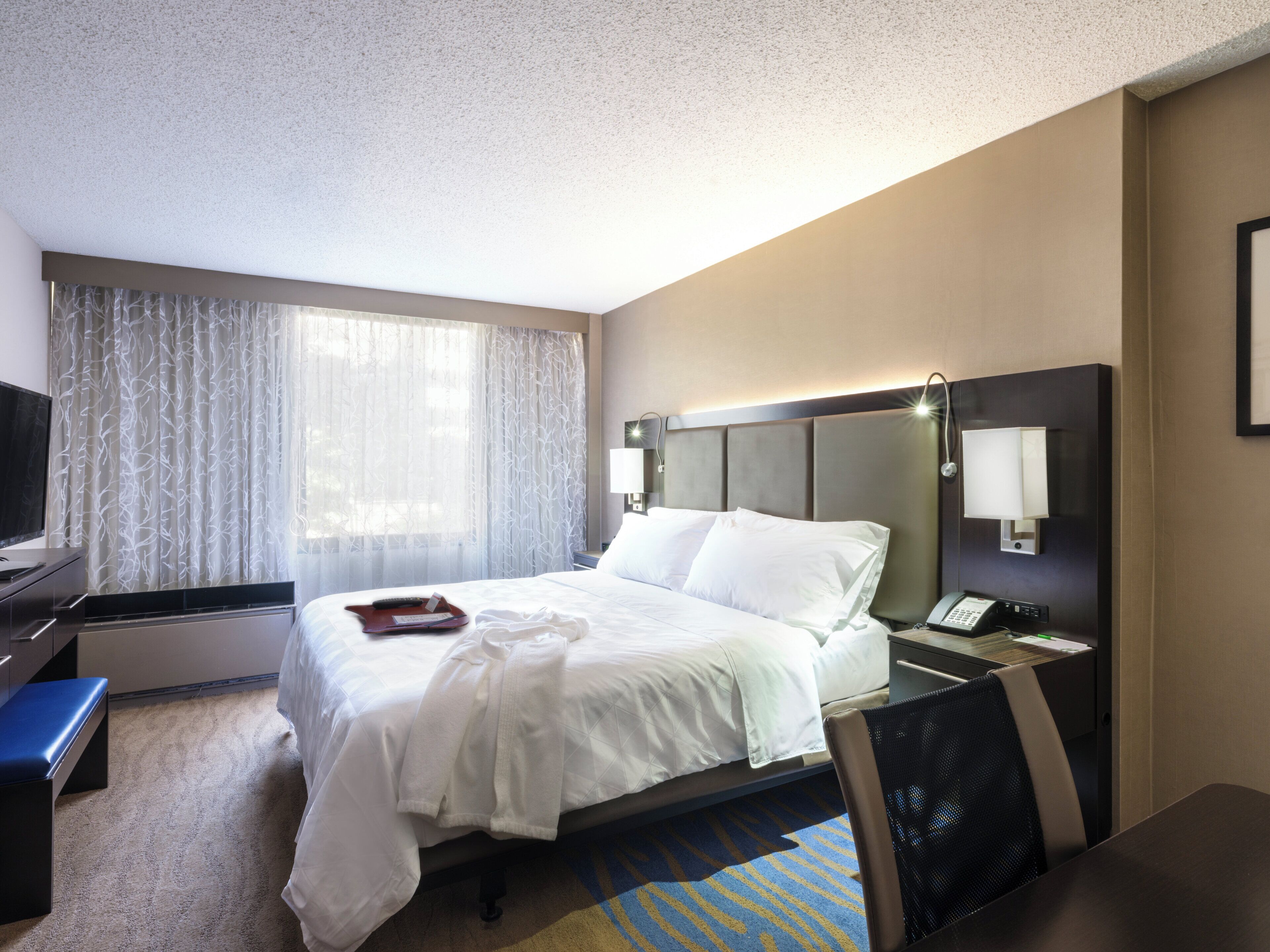 Una habitación de hotel con cama, mesita de noche, lámpara y un escritorio con silla.