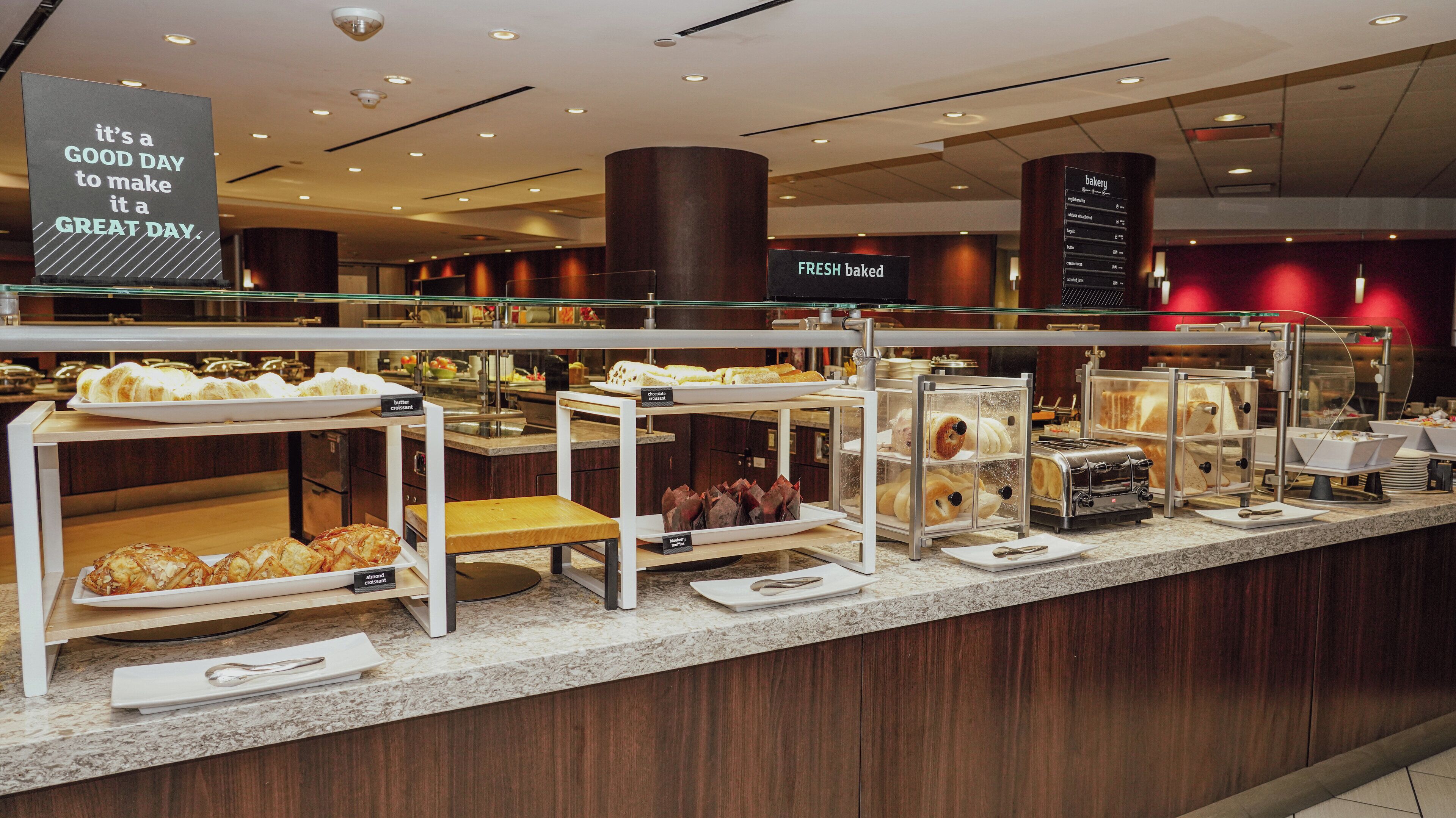 Una barra de panadería con diversos productos horneados exhibidos en vitrinas, como cruasanes, muffins y pasteles.