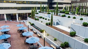 An outdoor patio area with multiple tables and blue umbrellas, surrounded by planters with greenery. - Holiday Inn Washington Capitol - Natl Mall by IHG (Washington)