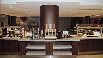 Ein Frühstücksbuffet mit Kaffeemaschine, Müsli und einer Auswahl an Früchten und Joghurt.