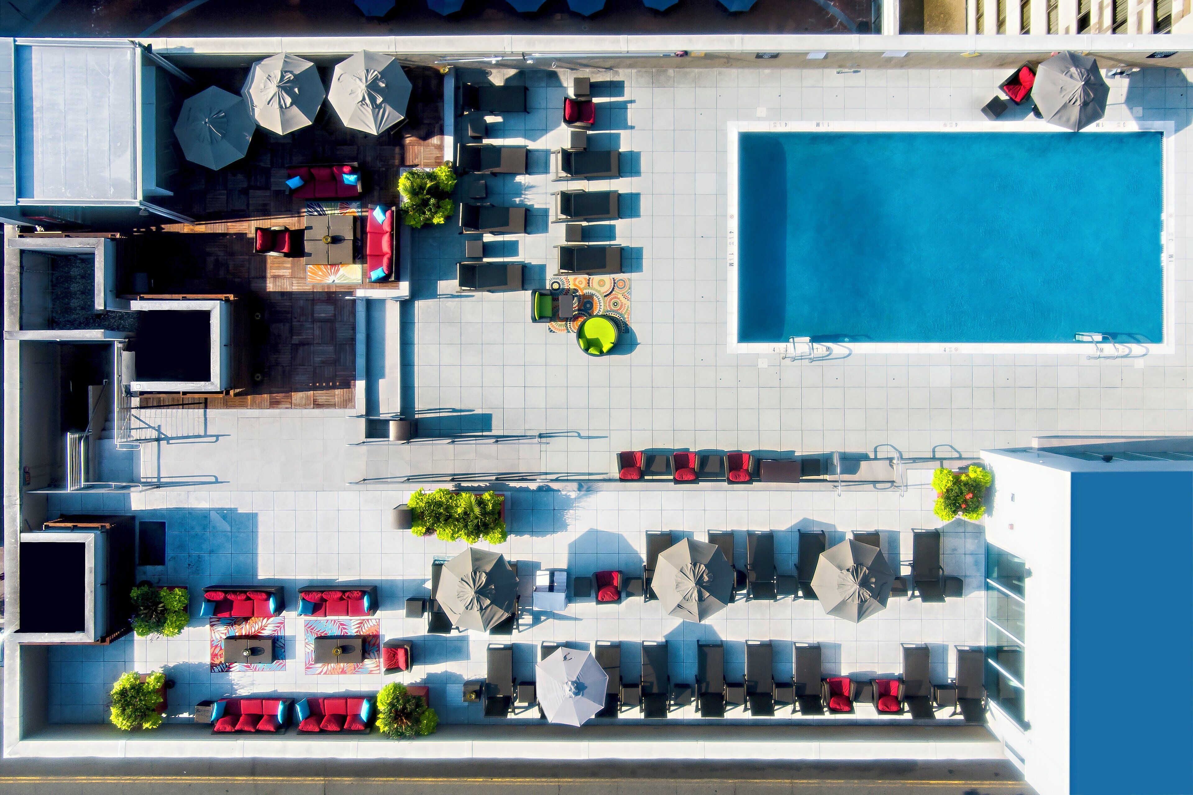 A rooftop pool area with multiple seating arrangements, umbrellas, and a swimming pool.