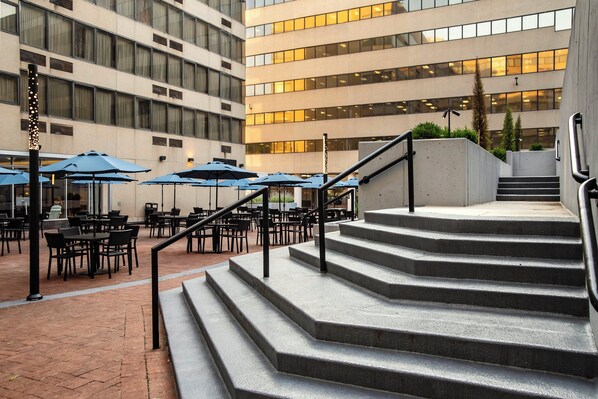 A building with multiple floors, outdoor seating area with tables and umbrellas, and a staircase leading to the upper levels.
